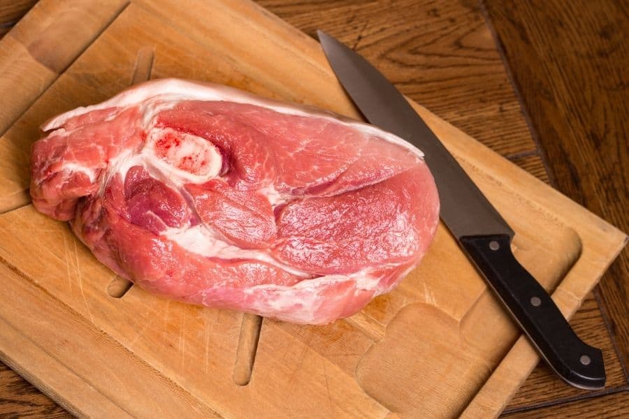 A piece of bone-in pork shoulder on a cutting board with a knife